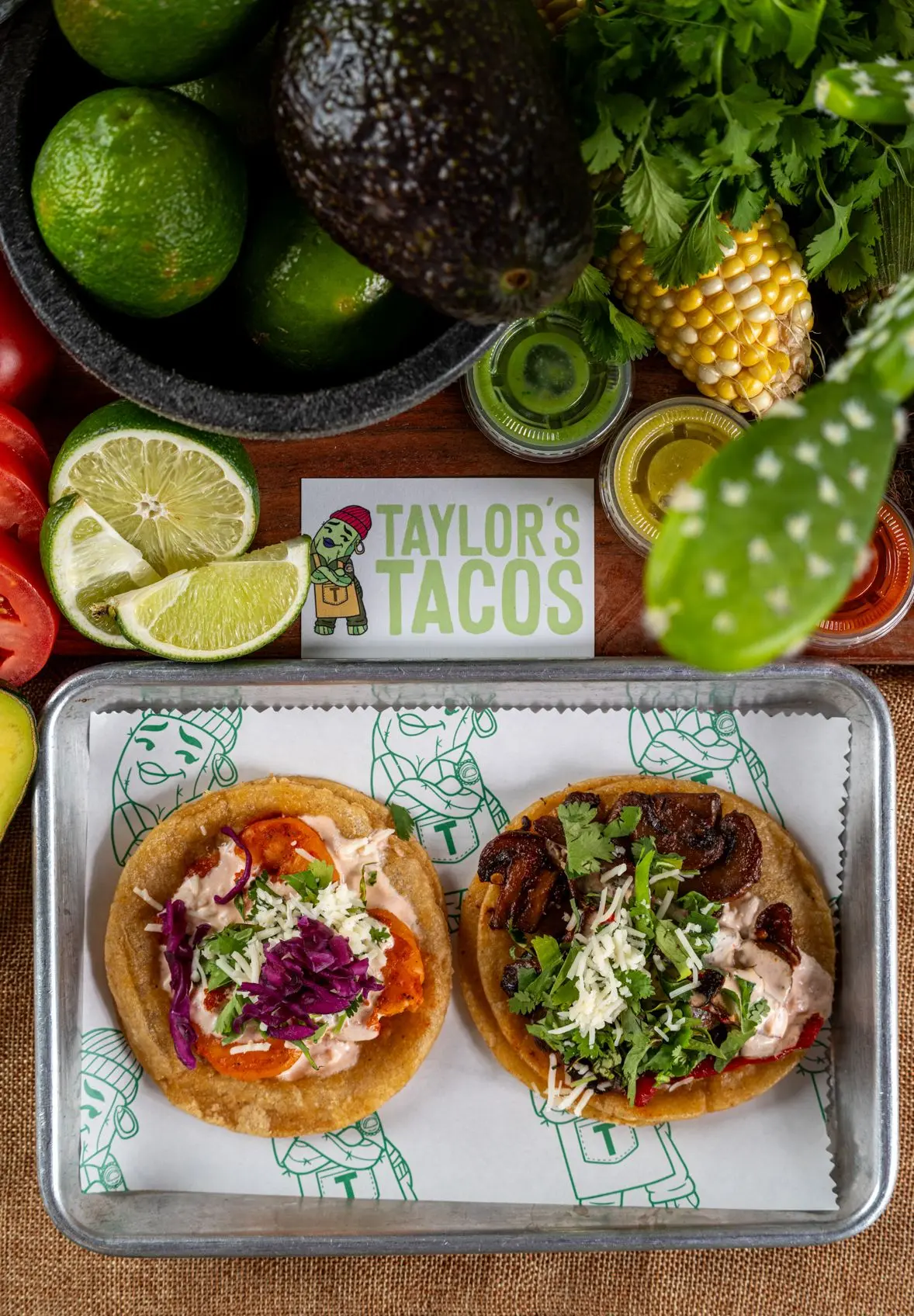 Taylor's Tacos Chicago overhead view of two signature tacos on a branded tray surrounded by fresh avocado, lime and cilantro